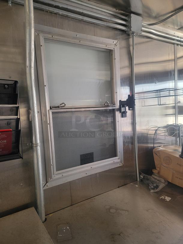 Metal-framed window with sliding glass and screen on a stainless steel wall, featuring a phone holder and nearby packages.