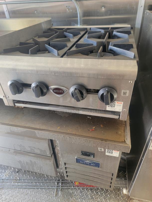 Wells four-burner commercial gas stovetop with control knobs, gently used. Below is an Arctic Air commercial refrigerator.