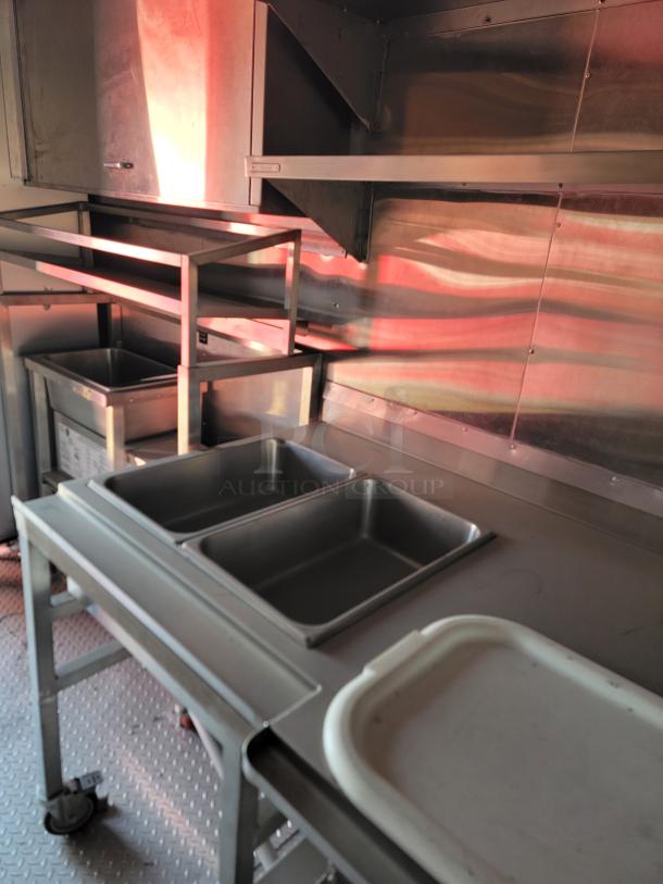 Commercial kitchen setup with stainless steel counters, shelves, and bins. Clean condition, ideal for food preparation.