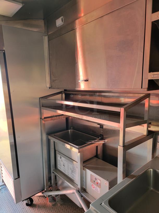Stainless steel kitchen equipment with shelving and a deep fryer. Features control panel and document holder, used condition.