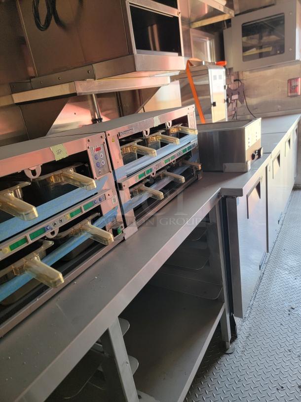 Industrial kitchen setup with multiple stainless steel ovens and food warmers. Visible control panels, safety markings, used condition.