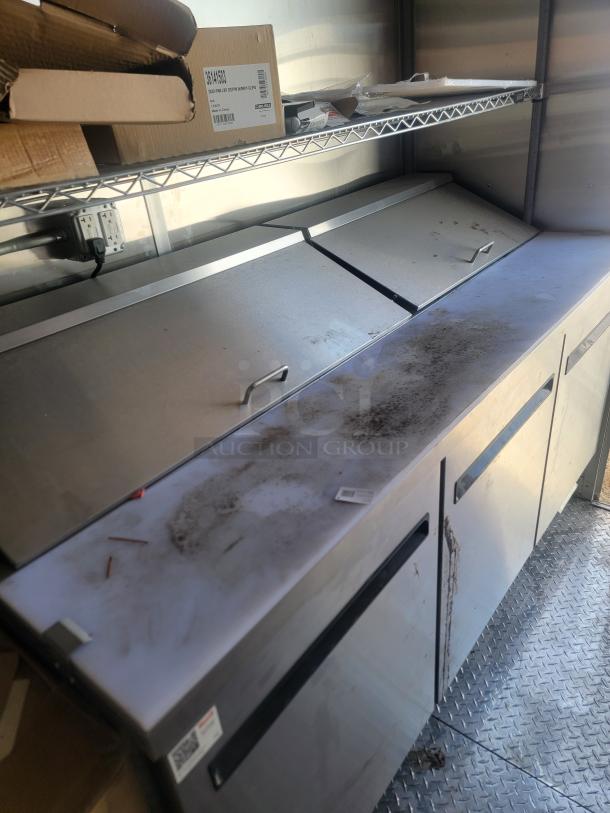 Commercial stainless steel prep table with top covers and storage below. Visible signs of wear and dirt. Suitable for kitchen or restaurant use.