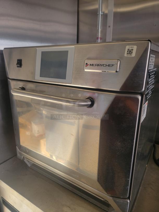 Stainless steel Merrychef commercial oven with digital display, visible scuffs. Model tag shows QR code and ID number 1012781.
