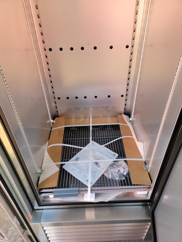 Commercial display refrigerator interior with shelving and instructions visible. New condition, metal and glass materials.