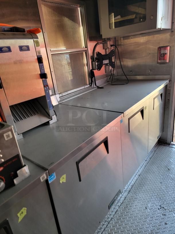 Commercial kitchen counter with stainless steel appliances, including a sliced sandwich prep unit and storage cabinets. Visible Crown Verity brand labels.
