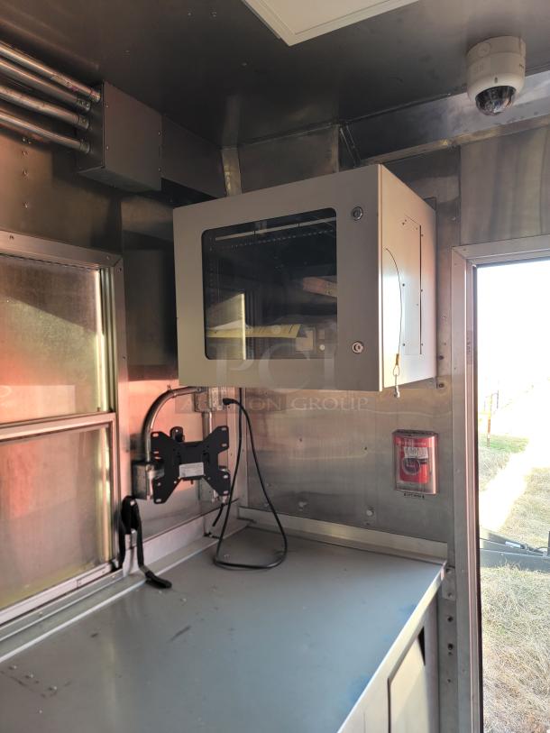 Industrial metal cabinet with glass-front door mounted on wall, adjacent to a security camera and fire alarm. Used condition.