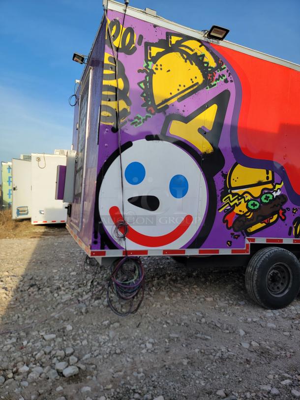 Colorful food truck side with taco and burger graphics, featuring a smiling face logo. Visible cables hang below.
