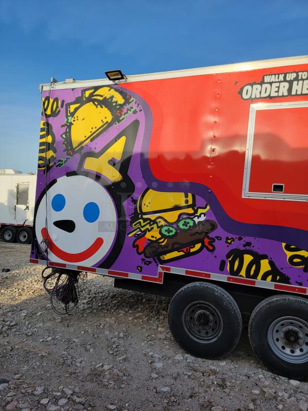 Colorful food truck with cartoon graphics, featuring a smiling face and food items. Red and purple design, dual rear wheels.