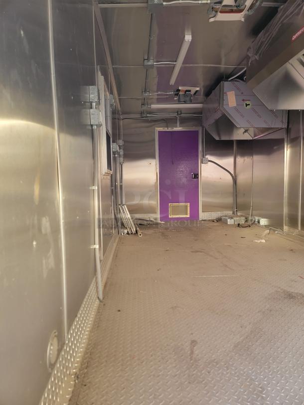 Interior of a stainless steel trailer with a diamond plate floor, purple door, electrical outlets, and ventilation system.