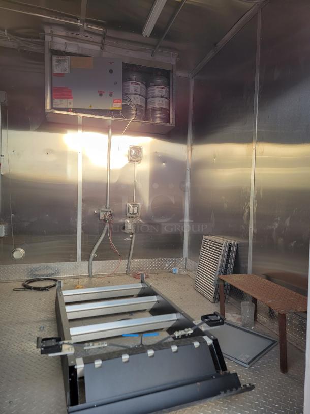 Industrial equipment room with mounted control panel, fire suppressant cylinders, and metal flooring. Components and tools visible.
