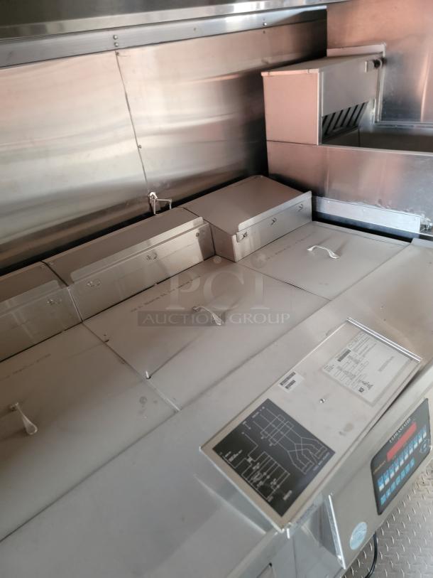 Commercial stainless steel food truck interior with warmers and storage, featuring control panel and circuit diagram label.