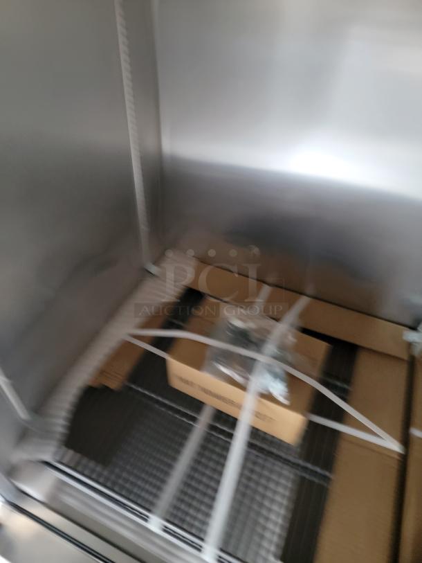 Stainless steel industrial cabinet interior with metal shelves, cardboard box, and plastic-wrapped components in excellent condition.