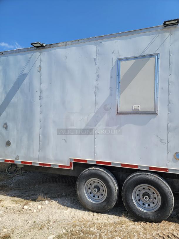 Enclosed utility trailer with metal siding, dual axles, and visible side hatch. Weathered condition, light wear marks.