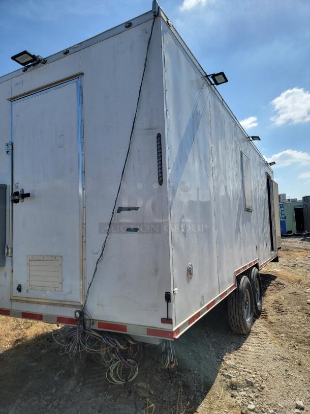Mobile utility trailer with dual axles and exterior lighting. Visible wear, wiring, and a rear door. No visible branding or model.