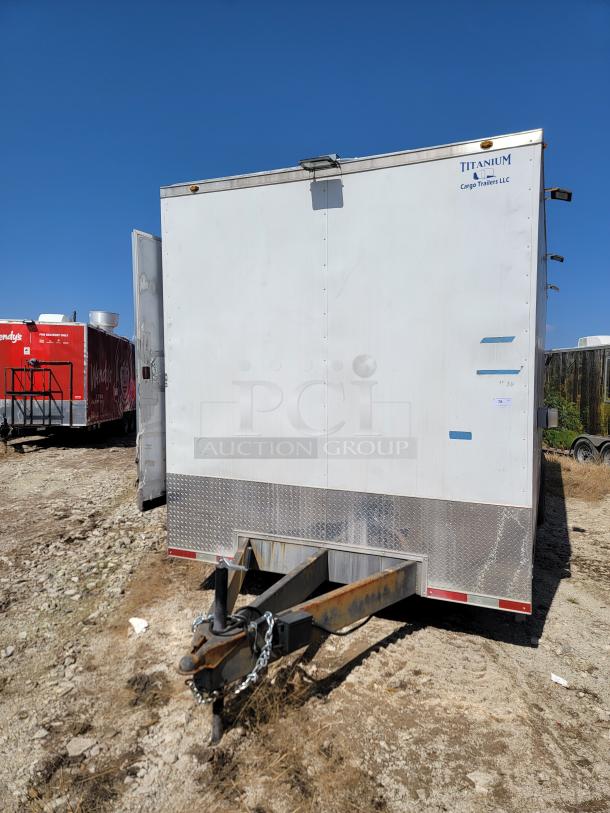 Titanium Cargo Trailer LLC white cargo trailer, diamond plate trim, visible rust on hitch; in used condition.
