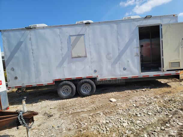 Mobile trailer with dual axles in fair condition, featuring an open door, rooftop vents, and external utility connections.