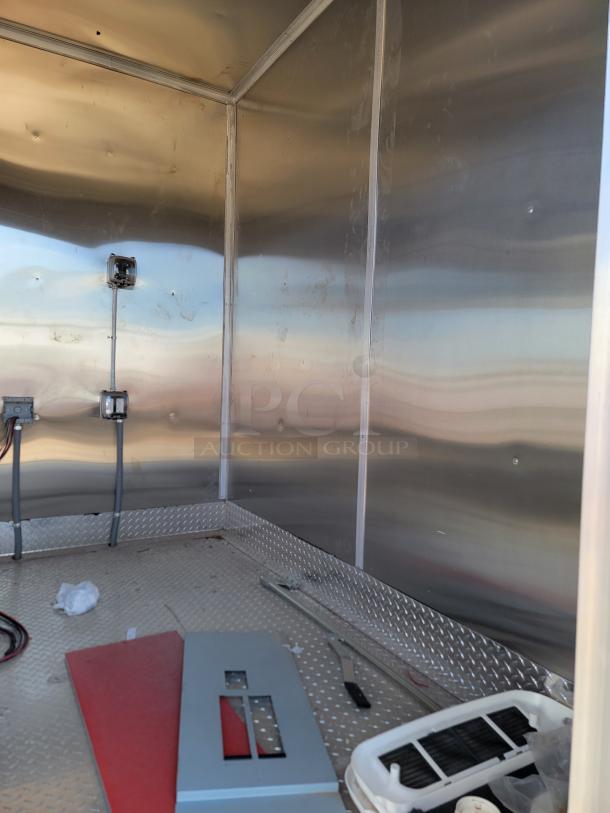 Interior of a metal utility trailer, shown empty. Features diamond plate flooring, electrical outlets, and wiring. Signs of wear visible.