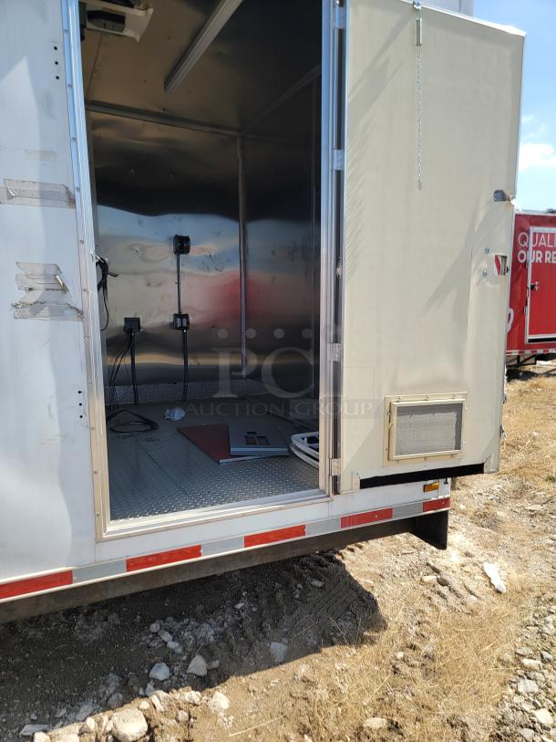 Enclosed trailer with an open side door, showing a stainless interior and utility outlets. Exterior has reflective tape.