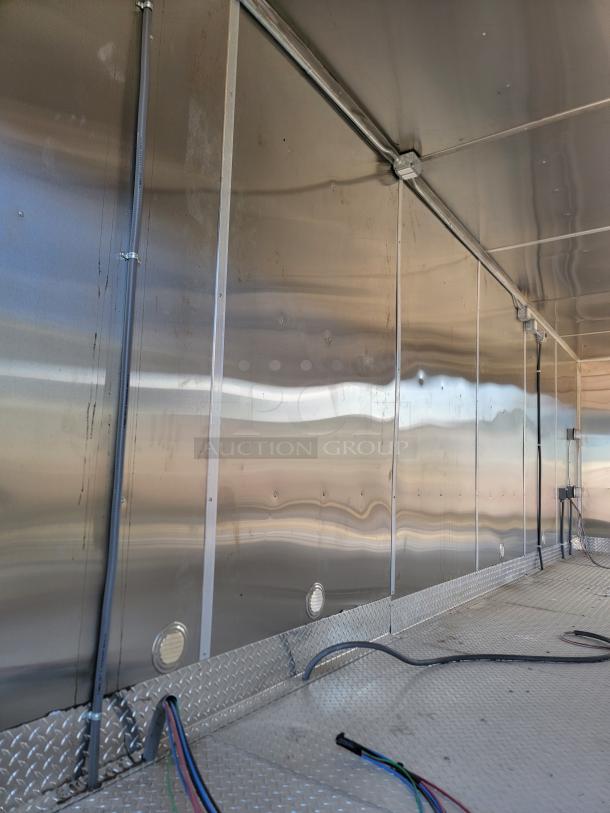 Interior of a metallic trailer showing sleek, shiny walls with wiring and diamond-plate flooring. New condition, no visible labels.