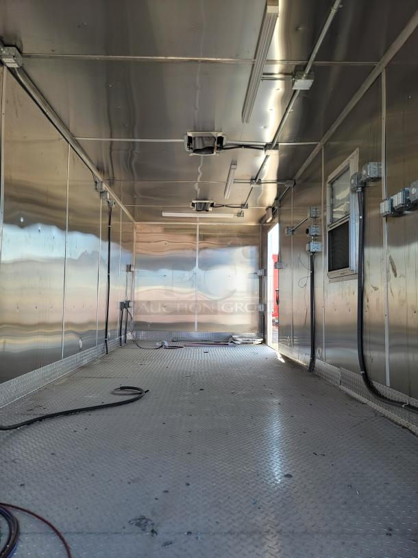 Empty industrial trailer interior with metal walls, ceiling, and flooring. Overhead lighting and electrical wiring visible.