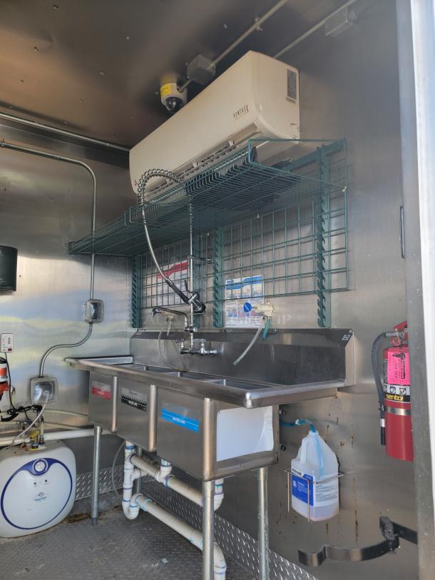 Stainless steel triple-basin sink with integrated faucet in a mobile unit. Features wall-mounted Ventus air unit and fire extinguisher.