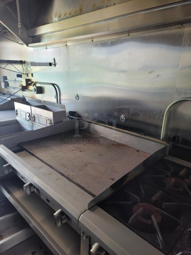 Commercial flat-top griddle with cast iron burners, stainless steel body. Used condition with visible wear marks.