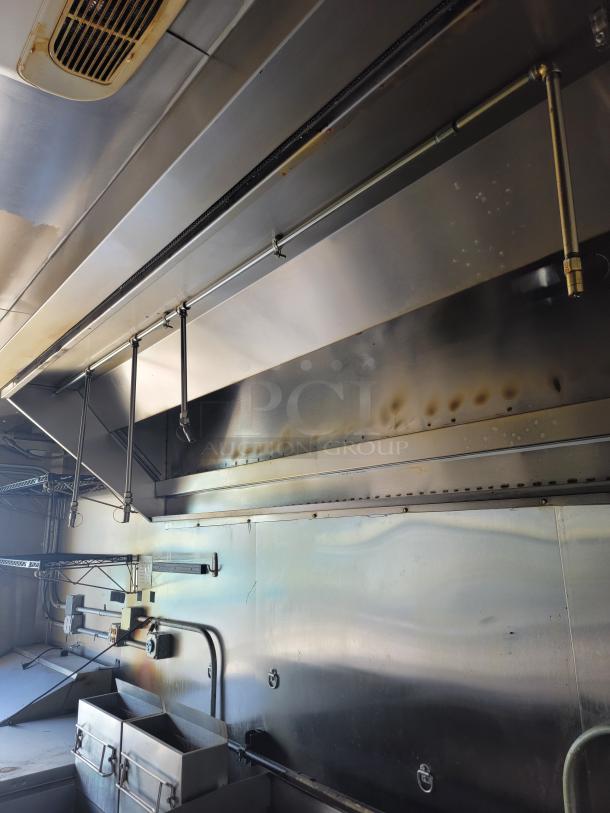 Industrial stainless steel commercial kitchen setup, featuring ventilation hood, overhead piping, and fry holders, in used condition.