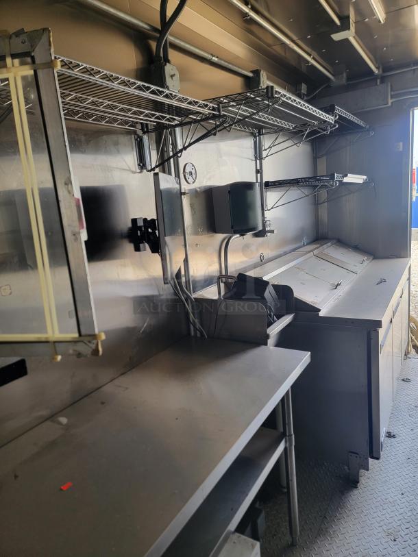 Industrial kitchen setup with stainless steel counters, shelving, and appliances. Features outlets and wiring. Condition appears used.