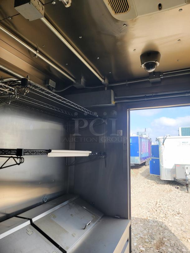 Stainless steel interior view of a mobile kitchen trailer with shelving, lighting fixture, and visible vent. Good condition.