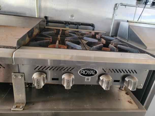 Royal commercial stovetop with four burners and griddle. Used condition, visible wear. Brand name and control knobs labeled.