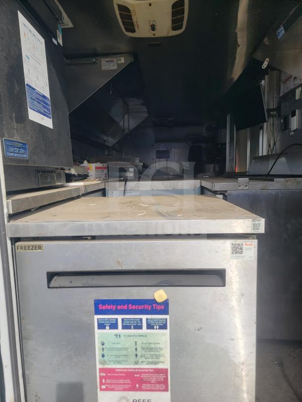 Interior view of 2013 Freightliner MT45 mobile kitchen, featuring Arctic Air freezer with safety tips label, Hoodz system visible.