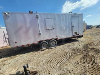 White mobile trailer on dual-axle wheels with utility hookups and vent, set on a dirt lot under a sunny sky.