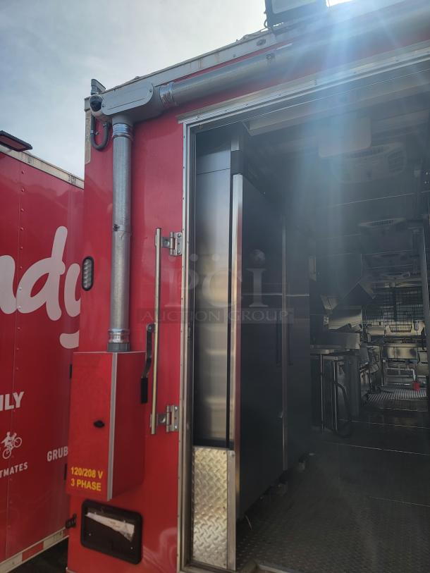 Red food truck with stainless steel kitchen appliances, open door, visible 120/208 V 3 phase marking.