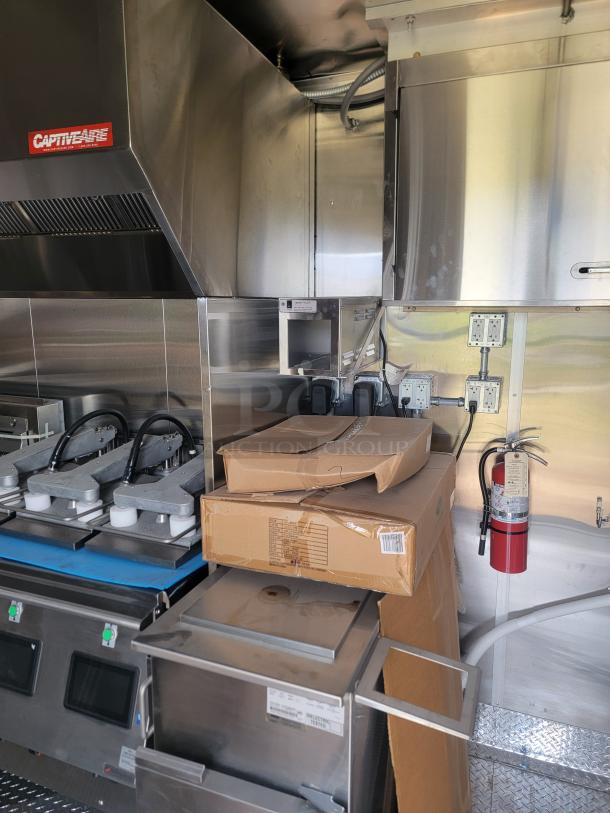 Commercial kitchen equipment in stainless steel with unassembled parts in boxes. CaptiveAire ventilation hood visible.