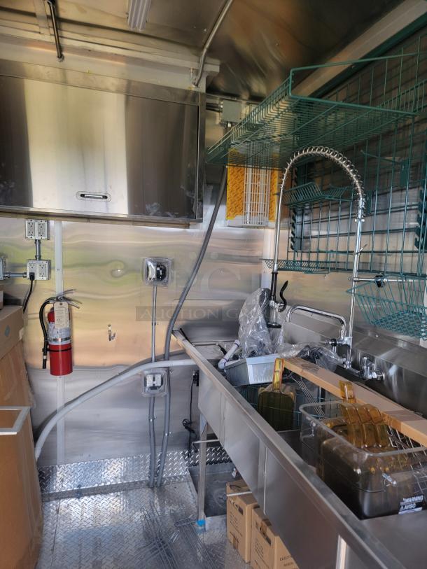 Commercial kitchen interior with stainless steel sink, industrial shelving, and fire extinguisher. Clean and ready for use.