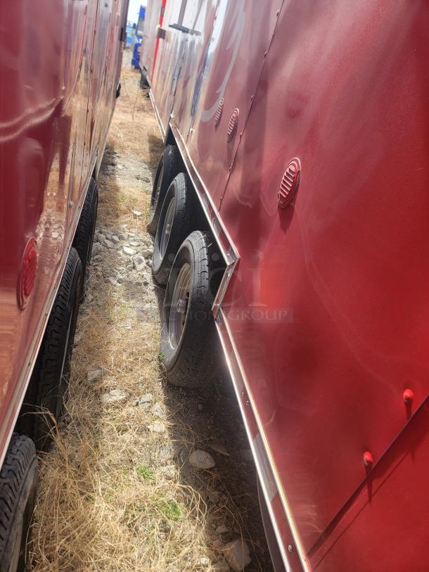 Red trailers with dual axles parked side by side on gravel and dry grass, showing vents and wheel details.