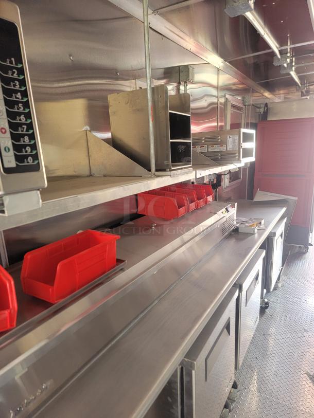Mobile workspace interior with stainless steel counters, shelves, and red storage bins. Well-lit, clean condition.