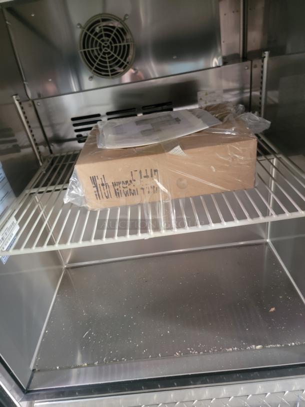 Cardboard box labeled "With wrench 51449" inside stainless steel container with fan and shelves. Box wrapped in plastic.