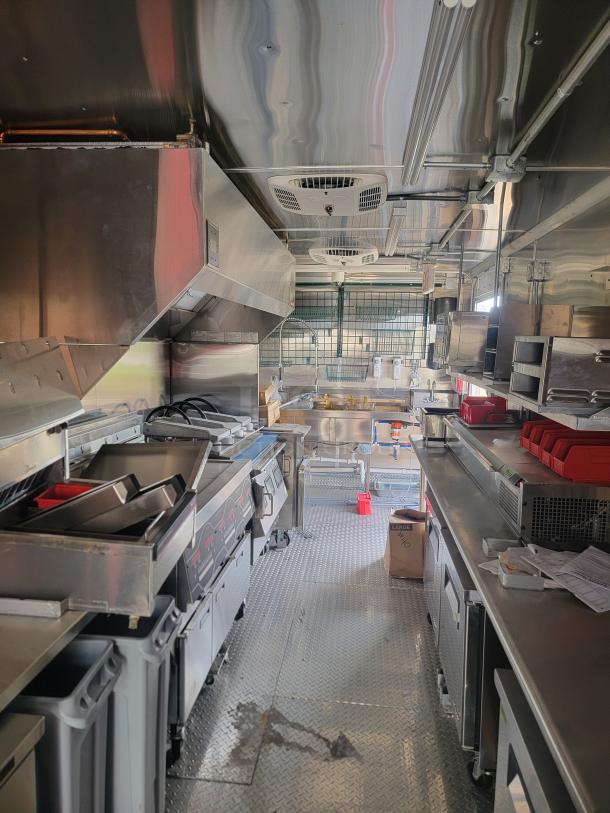 Commercial food truck interior with stainless steel appliances, including fryers and grills. Clean and well-maintained condition.