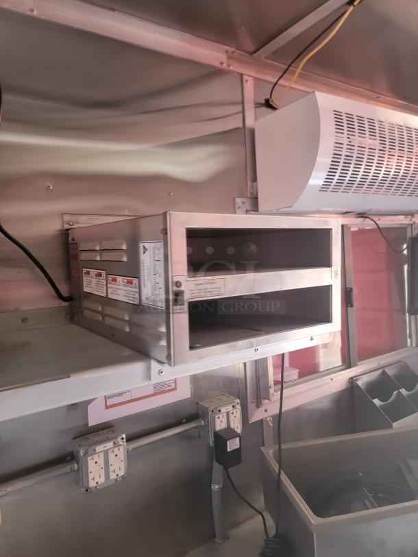 Stainless steel food warming oven, wall-mounted, with dual compartments, visible electrical wires, and safety instruction labels.