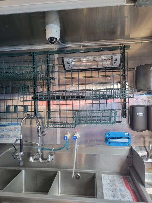 Commercial stainless steel sink setup with double basin, industrial faucet, wire racks, and sanitation dispensers.