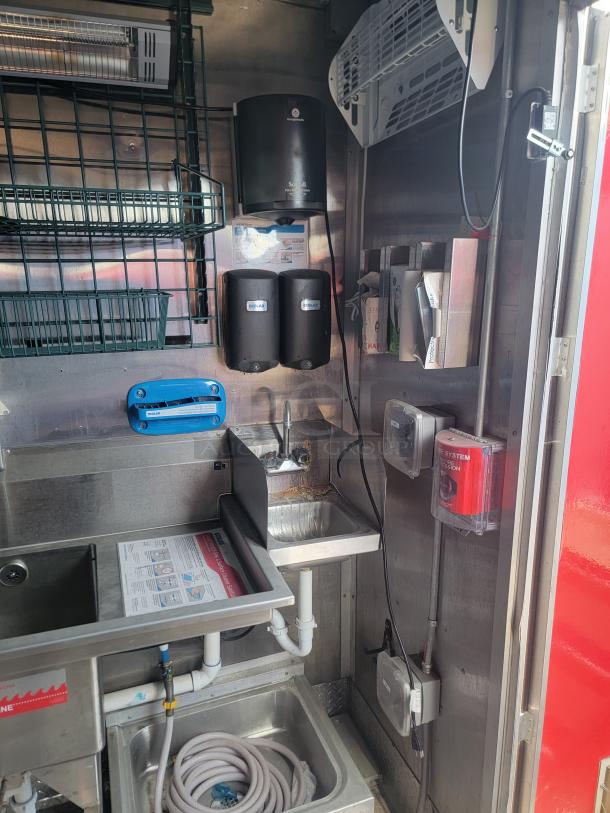 Commercial kitchen setup with stainless steel sinks, wall-mounted soap dispensers, a hand dryer, and an emergency fire system.