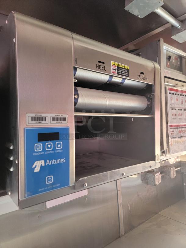 Antunes commercial toaster in stainless steel, with visible control panel for programming and browning. Labels indicate "Heel" and "Crown" rollers. Serial numbers present.