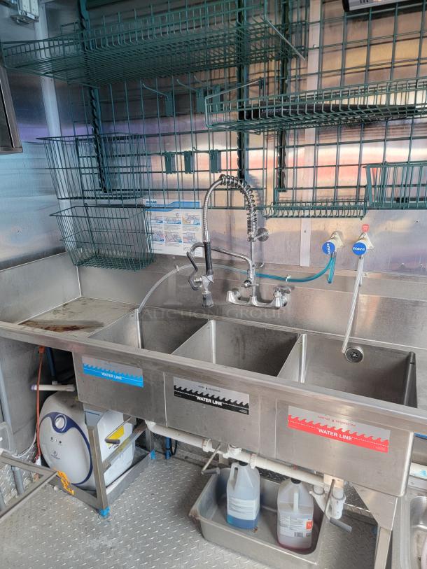 Stainless steel triple sink station with faucet, labeled for wash, rinse, sanitize. Includes shelving and Ecolab sanitizer controls.
