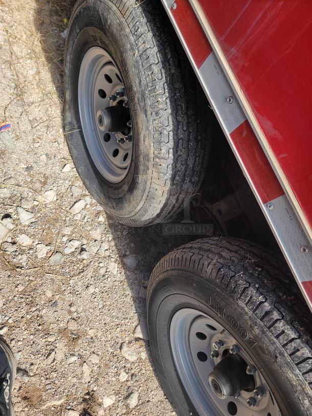 Dual trailer wheels with steel rims, marked "LH-001," attached to a red trailer. Condition appears used.