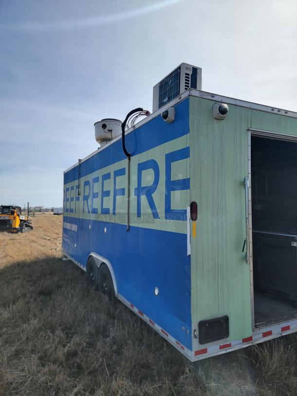Blue and green mobile refrigeration trailer with cooling unit, visible wear, vent and wiring on top, partially open rear door.