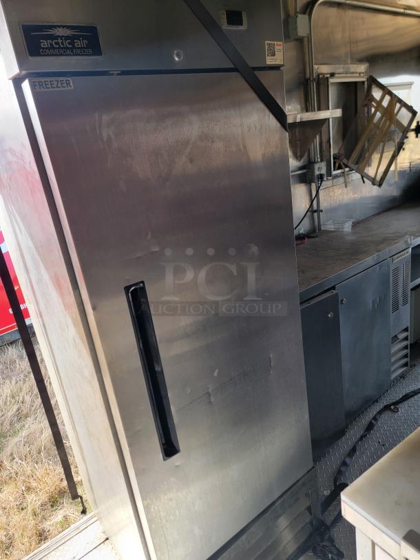 Arctic Air Commercial Freezer, stainless steel, upright model. Features a single door with a handle and visible wear.