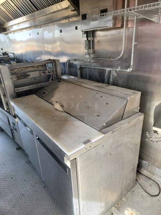 Commercial stainless steel prep table with refrigerated base, used condition, visible surface stains, two-door storage.