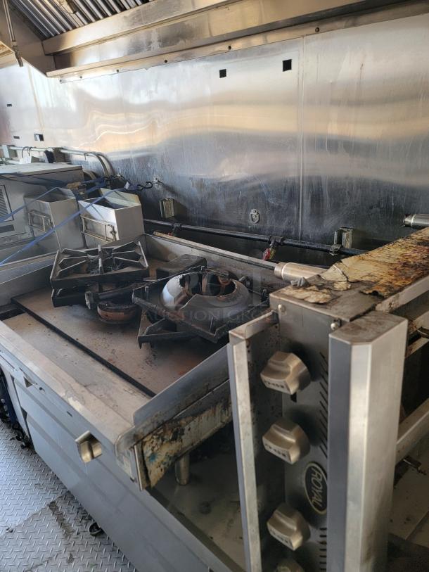 Commercial stovetop with two burners, stainless steel, worn condition, visible grease stains, Roval brand knobs.