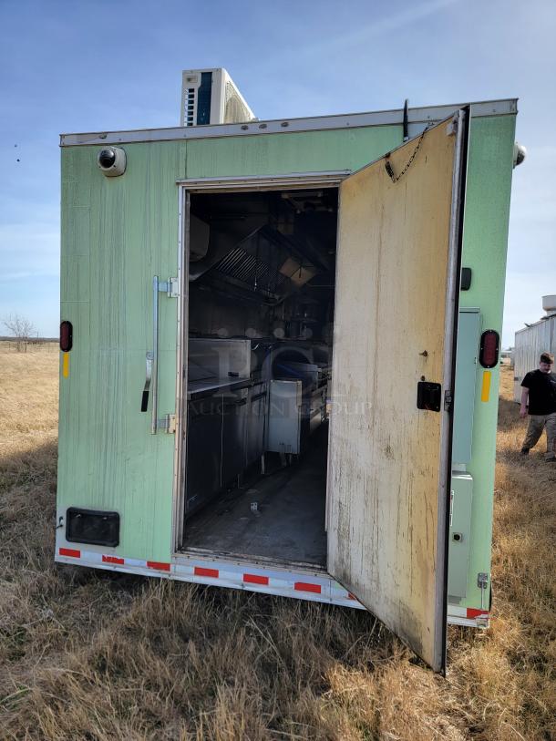 Mobile kitchen trailer with side door open, showing interior stainless-steel appliances. Exterior light green with visible wear.